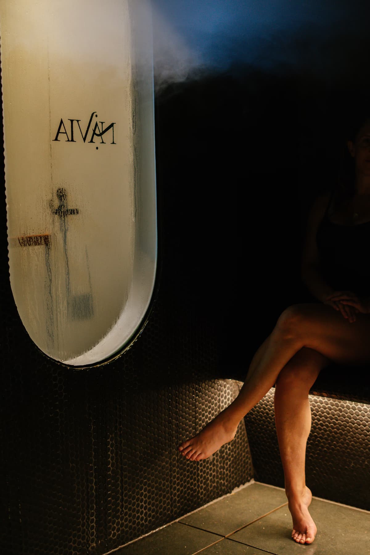 Bather resting in the steam room behind Navia's fogged porthole window