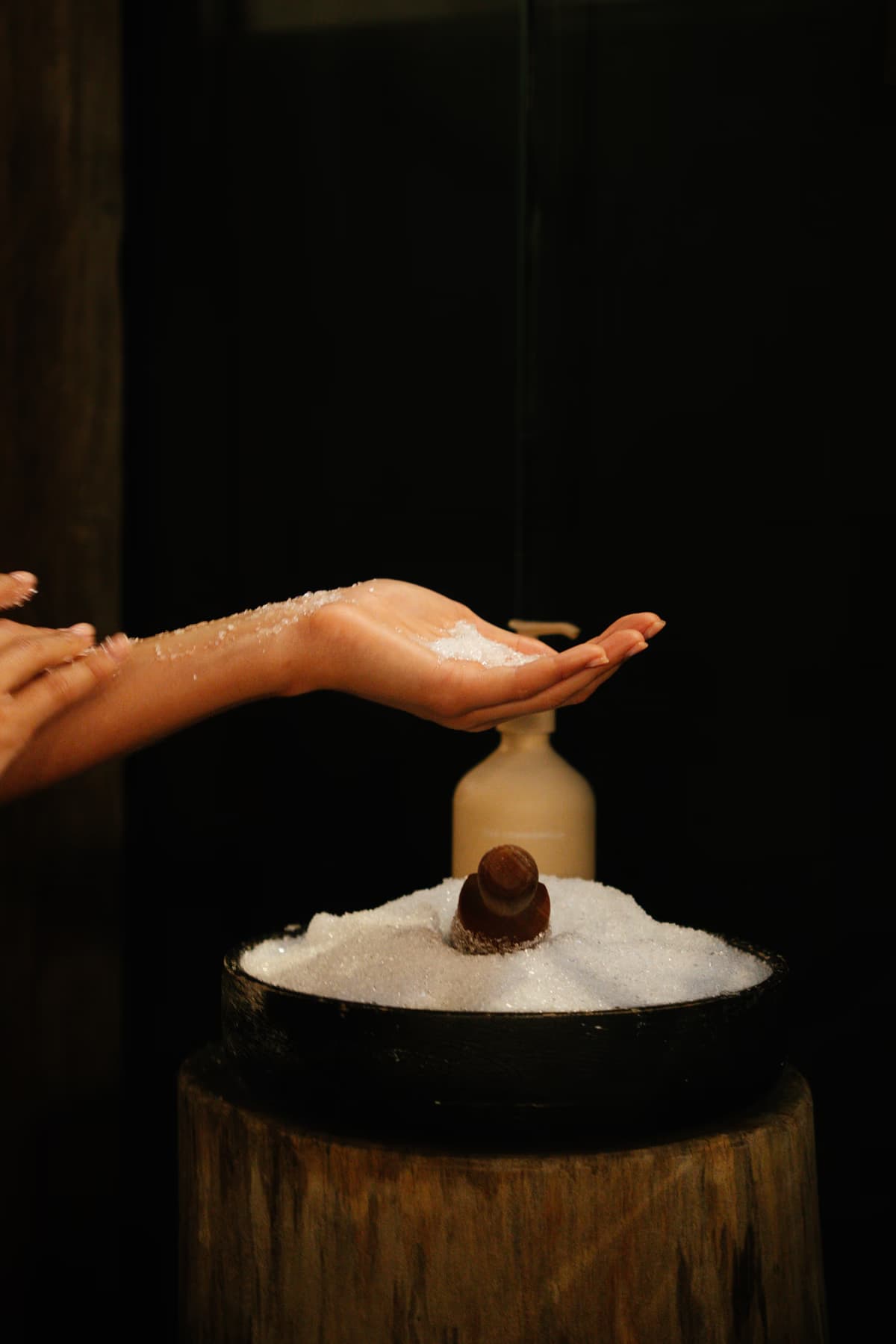 Hands cupping Navia's signature magnesium salt scrub beside an amber bottle on a timber stand