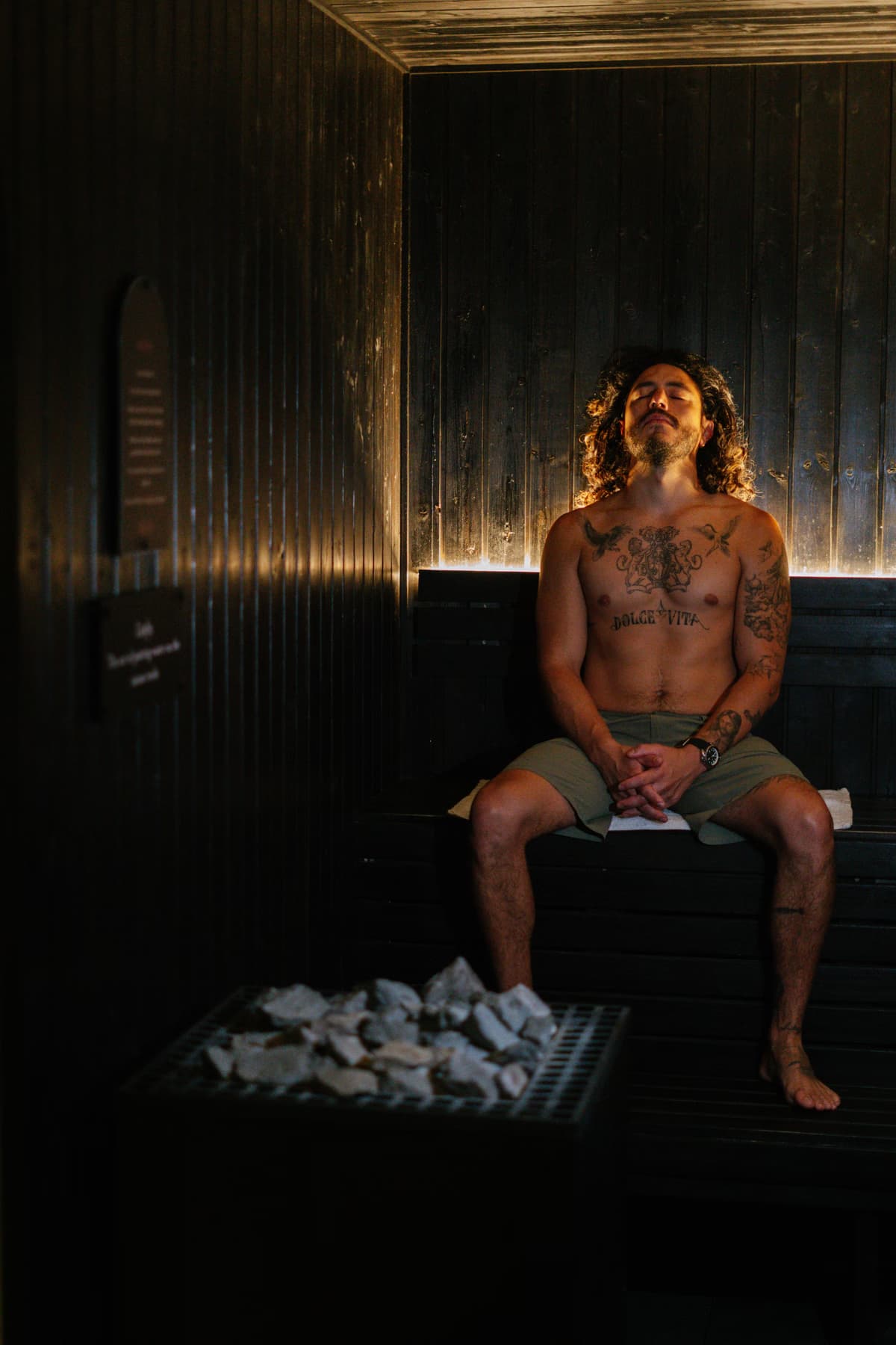 A bather resting on the bench of the warm timber sauna at Navia Bathhouse, eyes closed