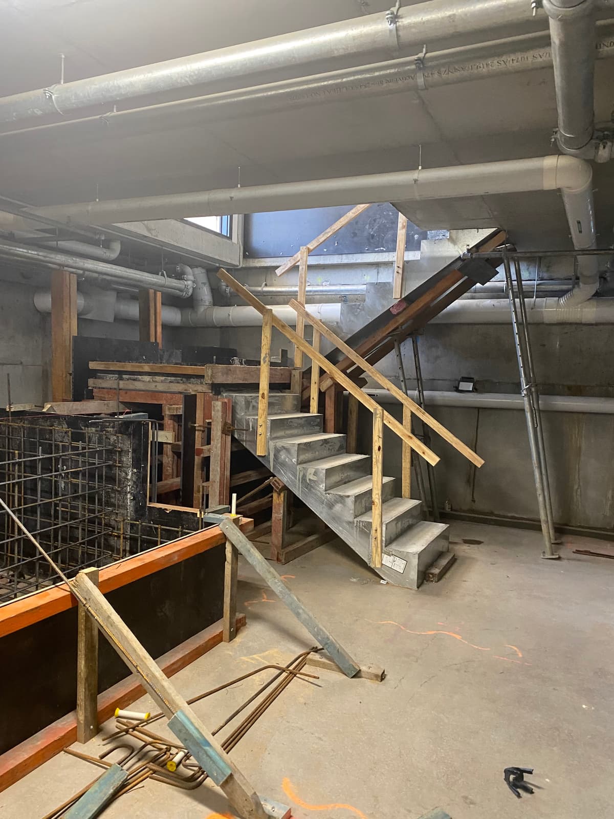 A concrete stairwell under construction below street level at Navia Byron Bay, timber formwork and exposed services around it