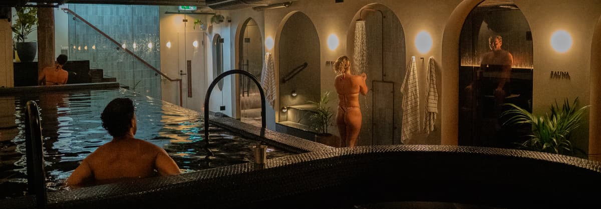 Evening view across the dark mineral pool and arched bathing alcoves at Navia Bathhouse