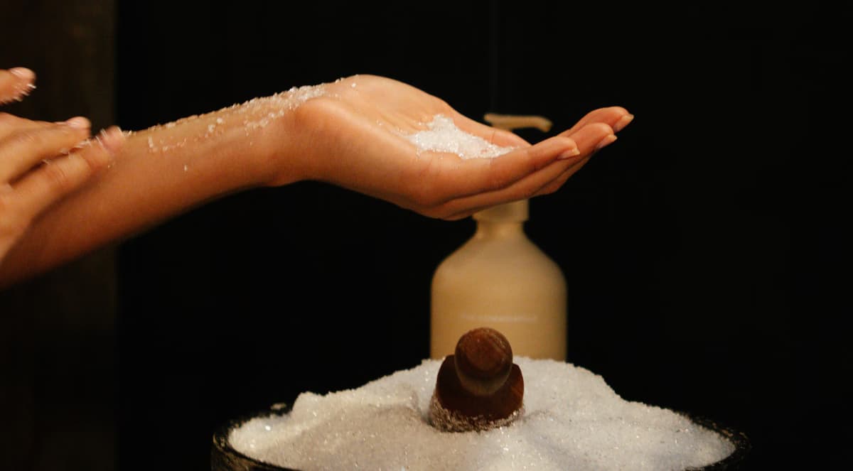 Cupped hands holding magnesium salt scrub above a bowl of salt beside an amber bottle at Navia Bathhouse