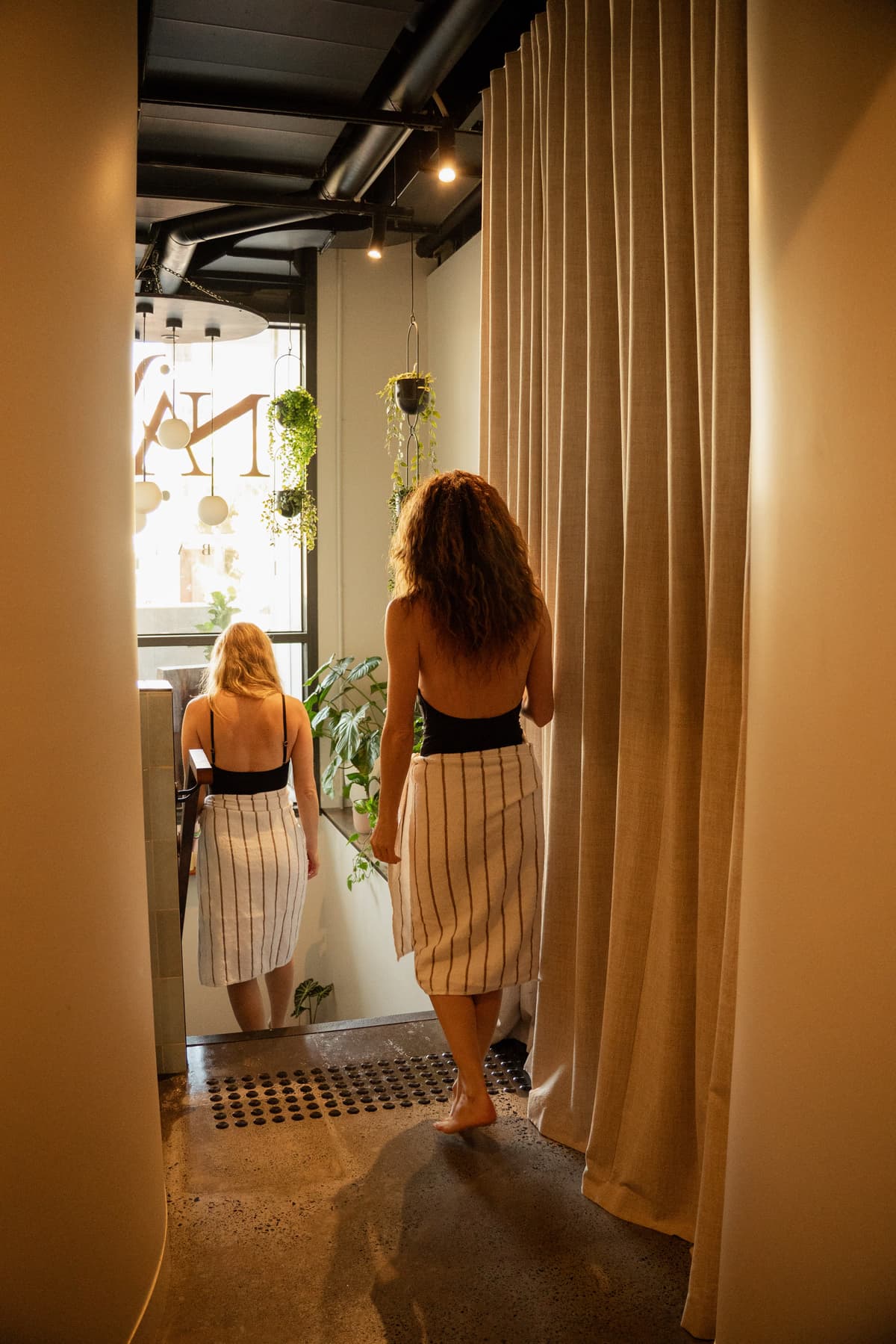 A guest in a bathhouse towel walking through the curtained corridor at Navia Bathhouse Byron Bay
