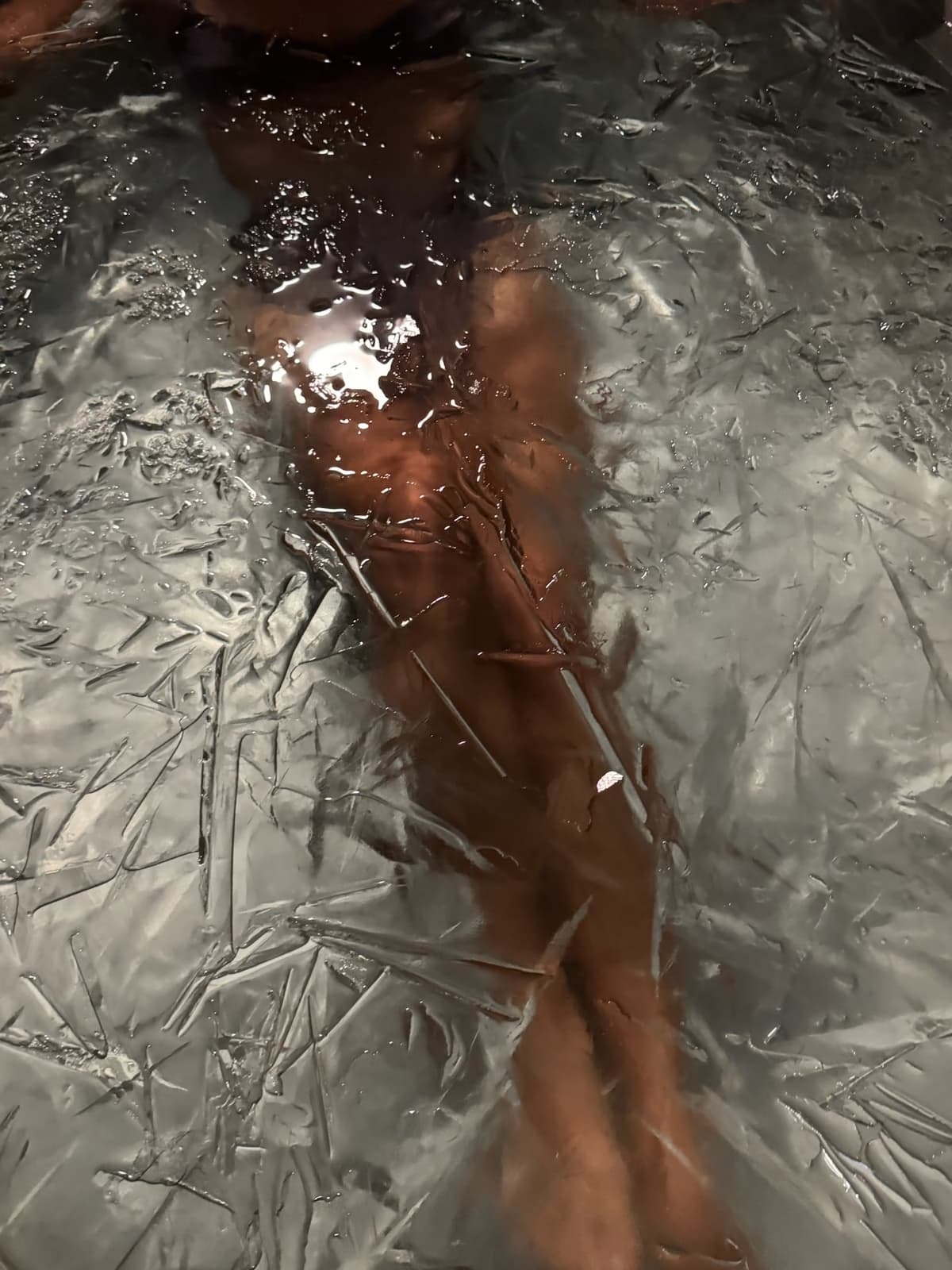 Bather submerged in the ice plunge at Navia Bathhouse, thin sheets of ice across the water's surface
