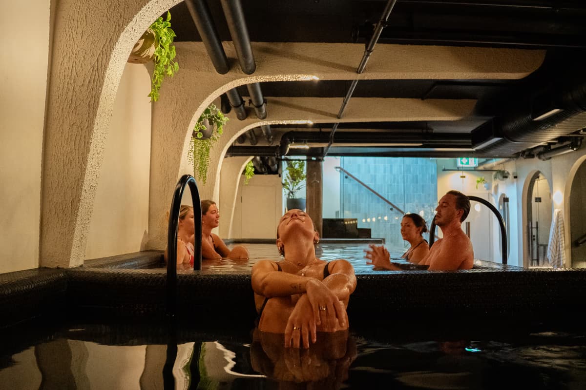 Bathers resting with legs raised in the dim cold plunge at Navia Bathhouse