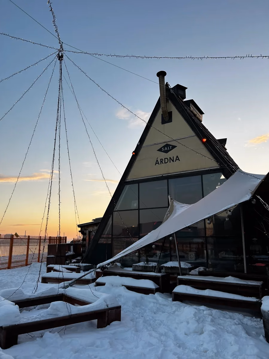 Glass-peaked Scandinavian bathhouse at golden sunrise with snow on the ground
